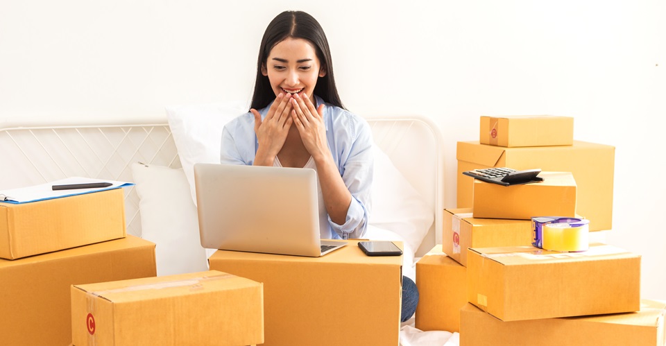 多くの梱包荷物とパソコン画面に向かって喜んでいる女性