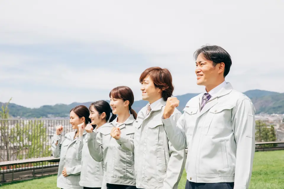 屋外でガッツポーズをとる5人の男女工員