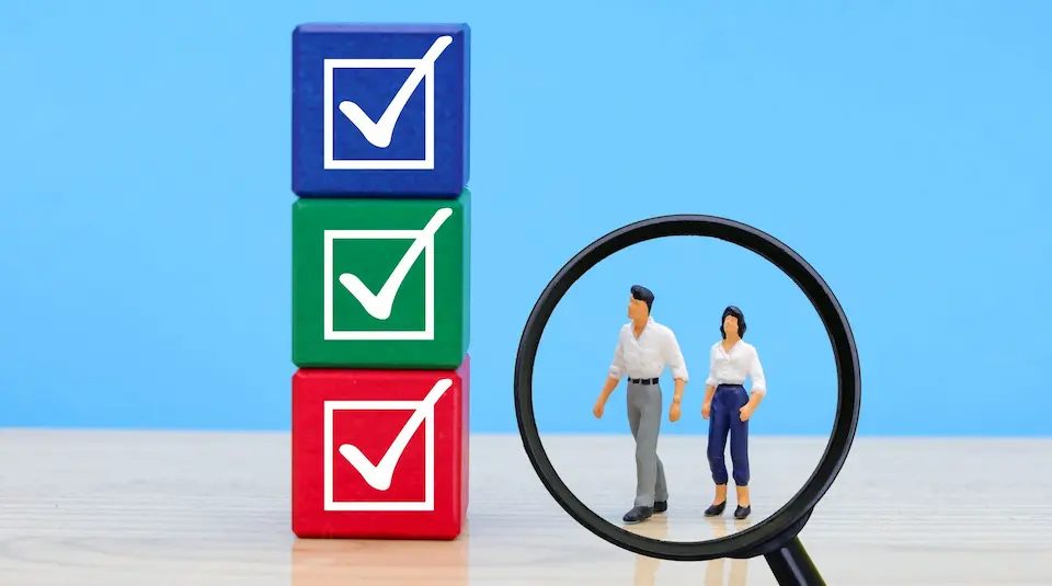 チェックマークの積み木を見上げる男女と虫メガネ