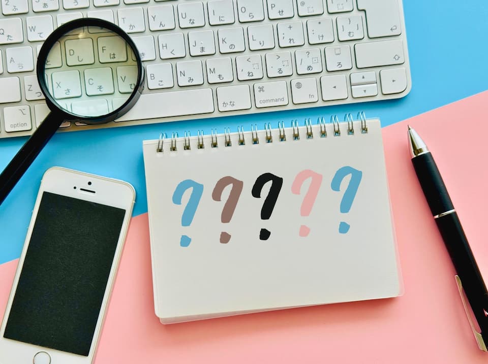 PCキーボード、ペン、スマホ、虫眼鏡とノートに書かれたはてなマーク