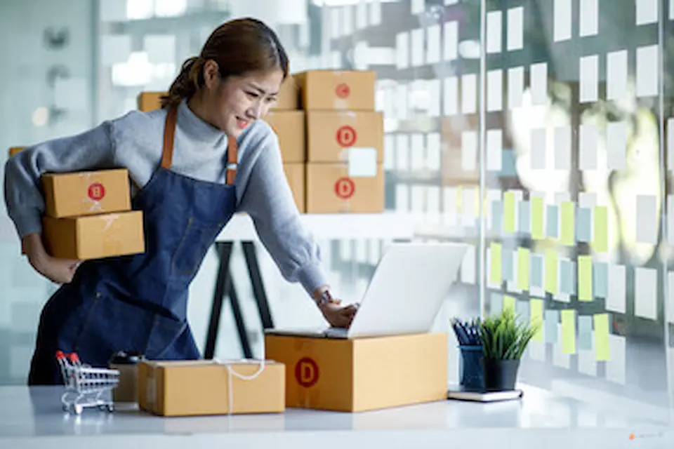 梱包商品を抱えてPCの画面を見る女性