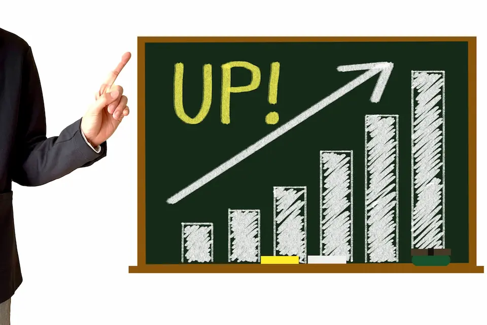 黒板に右肩上がりの棒グラフと、それを指さすビジネスマンの手